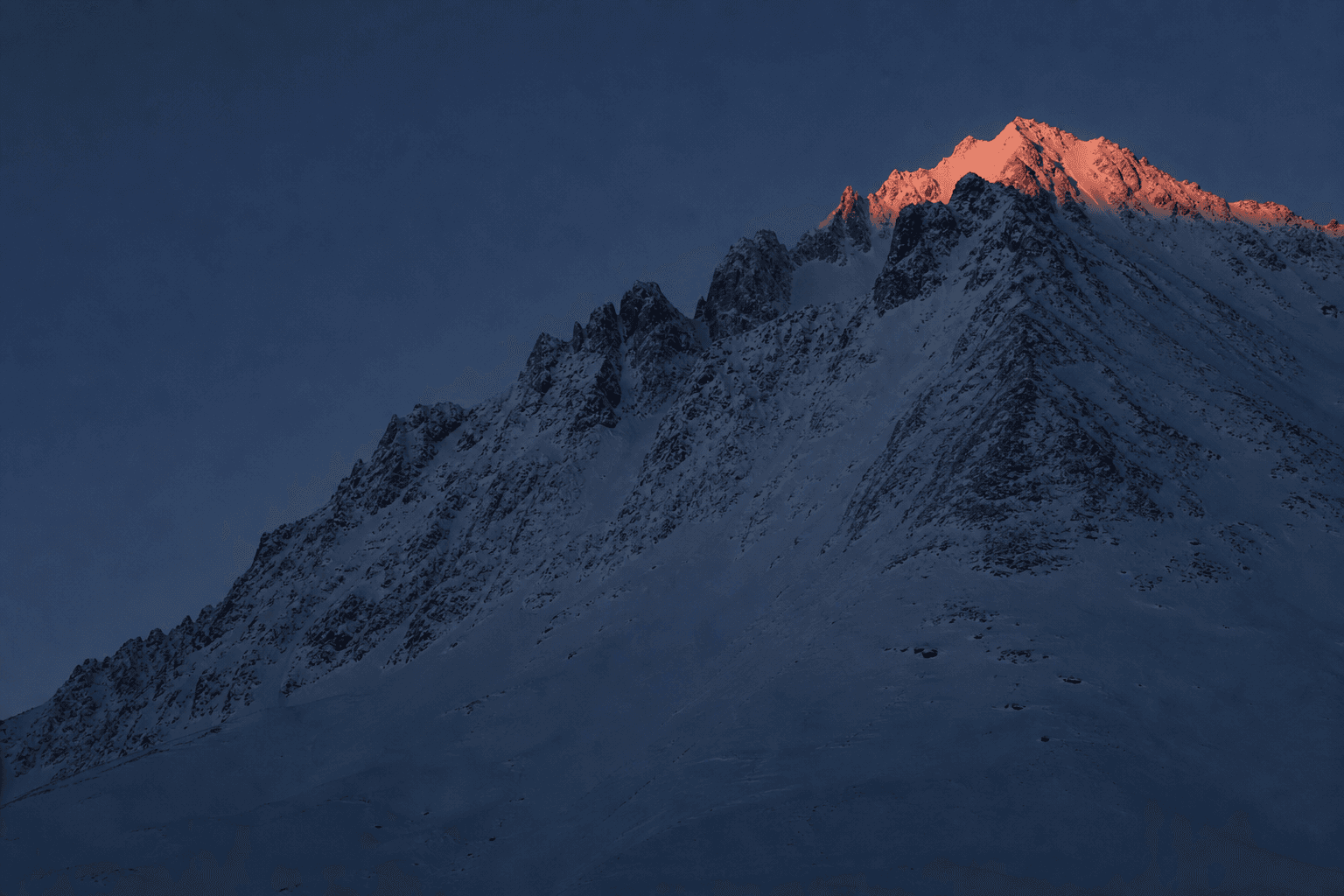 An alpine ridge in deep blue shadow with first light on the highest summit